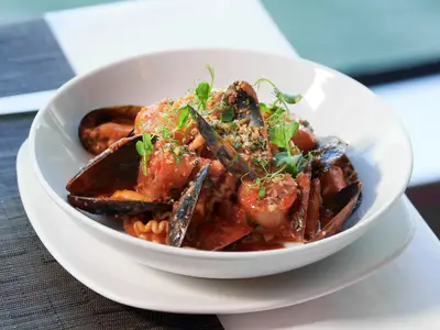 Eine weiße Schüssel mit frischer Pasta, Muscheln und Calamari im Restaurant Canaletto an Bord der Rotterdam.