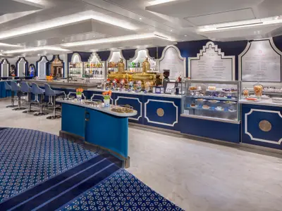 Innenansicht des Grand Dutch Cafe an Bord der Rotterdam mit einer blau-weißen Theke, Barhockern und Gebäckvitrine.