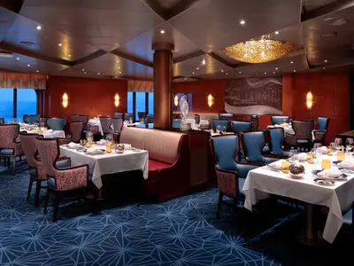 Stilvolles Restaurant an Bord der Rotterdam mit blau gemustertem Teppich, weiß eingedeckten Tischen und blauen Polsterstühlen.