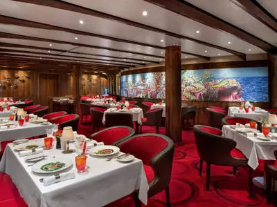 Elegantes Restaurant an Bord der Rotterdam mit rot-schwarzen Sesseln, weiß gedeckten Tischen und farbenfrohen Wandgemälden mit Meeresmotiven.