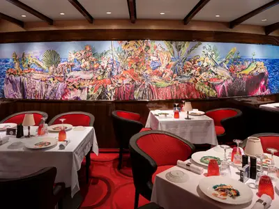 Elegant eingedeckte Tische und rote Sessel im Restaurant Rudi's Sel de Mer vor einem großen Kunstwerk an Bord der Rotterdam.
