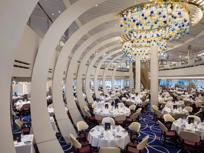 Das stilvolle, zweistöckige Restaurant an Bord der Rotterdam mit geschwungenen weißen Säulen und einem großen Glaskronleuchter.