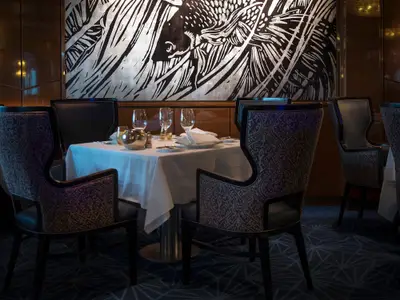 Ein festlich gedeckter Restauranttisch mit kunstvoll gemusterten Stühlen an Bord der Rotterdam.