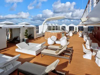 Ein moderner Außenbereich mit Whirlpool, Cabanas und weißen Liegestühlen an Bord der Rotterdam unter blauem Himmel.