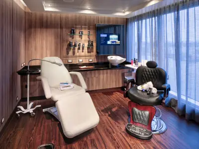 Ein moderner Friseur- und Spa-Salon an Bord der Rotterdam mit einem weißen Behandlungssessel und einem schwarzen Barbiersessel vor einer Holzwand.