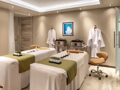 Ein moderner Spa-Behandlungsraum für Paare an Bord der Rotterdam mit zwei Massagebänken und Bademänteln.