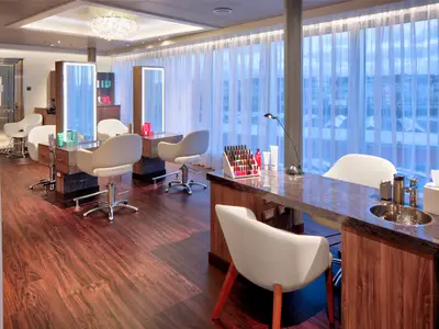 Ein eleganter Friseursalon und Maniküre-Arbeitsplatz an Bord der Rotterdam mit weißen Sesseln, großen beleuchteten Spiegeln und Holzfußboden.