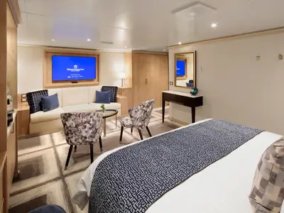 Innenansicht einer luxuriösen Suite an Bord der Rotterdam mit einem Doppelbett im Vordergrund sowie einer Sitzecke.
