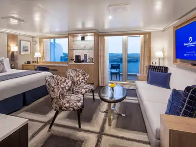 Eine luxuriöse Suite an Bord der Rotterdam mit Doppelbett, gemütlichem Sofa, Sesseln, Flachbildfernseher und Balkonzugang mit Meerblick.