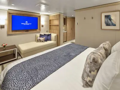 Schlaf- und Wohnbereich einer luxuriösen Suite an Bord der Rotterdam mit großem Bett, Sofa und TV-Bildschirm.