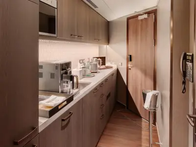 Pantrybereich in einer Suite an Bord der Rotterdam mit Kaffeemaschine, Spülbecken, Arbeitsplatte aus Stein und edlen Holzschränken.