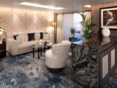 Blick in den eleganten Wohnbereich der Pinnacle Suite an Bord der Rotterdam mit weißem Sofa, flauschigem Sessel und stilvoller Bar.