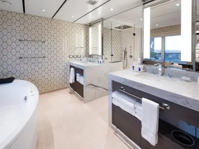 Elegantes Badezimmer der Pinnacle Suite an Bord der Rotterdam mit Marmor-Doppelwaschtischen, einer Badewanne und luxuriösen Wandfliesen.