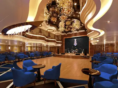 Blick in die elegante Queen's Lounge an Bord der Rotterdam mit Tanzfläche, blauen Polstersesseln und einer Musikbühne.