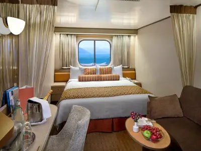 Eine gemütliche Außenkabine an Bord der Volendam mit einem großen Doppelbett, Meerblick durch ein Fenster und Sektkühler im Vordergrund.