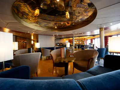 Blick in die stilvoll eingerichtete Ocean Bar an Bord der Volendam mit gemütlichen Sesseln und blauen Sofas.