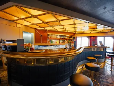 Die stilvolle Ocean Bar an Bord der Volendam mit einem geschwungenen Tresen, gemütlichen Barhockern und einer warm beleuchteten Decke.