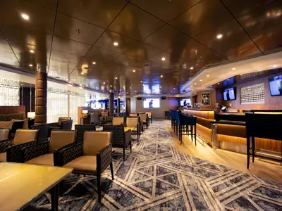 Die stilvolle Spirits & Ales Bar an Bord der Volendam mit dunklen Sesseln, Bartheke und Monitoren.