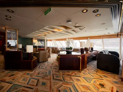 Blick in die stilvolle Crow's Nest Lounge an Bord der Volendam mit bequemen Sesseln, Teppichboden und großen Panoramafenstern.