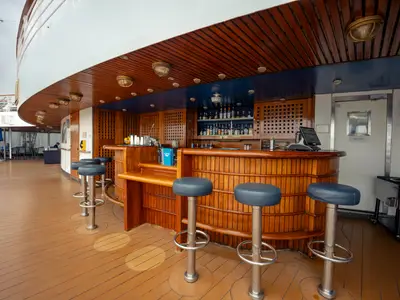Eine maritime Holzbar an Bord der Volendam mit blauen Barhockern und Flaschenregal im Hintergrund unter einem Holzdeck.