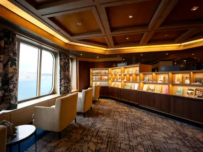 Einladender Lesebereich an Bord der Volendam mit gemütlichen Sesseln, Fensterfront zum Meer und Bücherregalen.