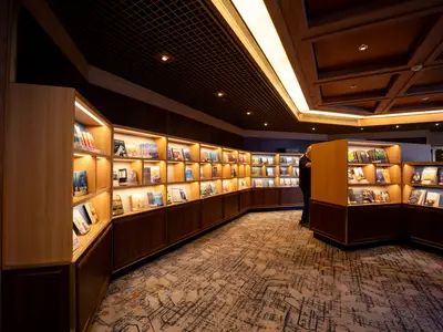 Gut sortierte, beleuchtete Bücherregale aus Holz in der gemütlichen Bibliothek an Bord der Volendam.