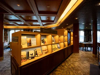 Ein beleuchtetes Bücherregal der Kategorie 'Short Stories' in der gemütlichen Bibliothek an Bord der Volendam.