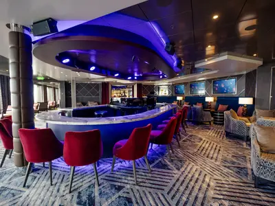 Die stilvolle Piano Bar an Bord der Volendam zeigt rote Barstühle an einem geschwungenen Tresen unter violettem Licht.