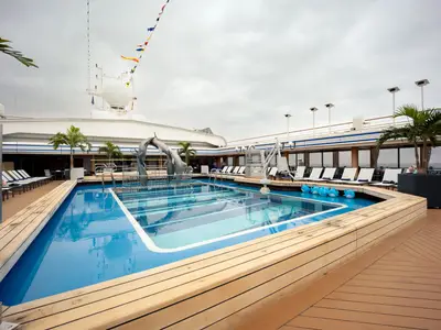 Blick auf den Lido-Pool an Bord der Volendam mit blauer Poolfläche, einer Delphinschulptur und Liegestühlen auf dem Außendeck.