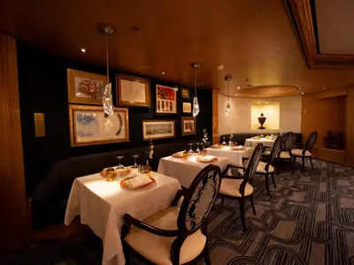 Eingedeckte Tische und elegante Polstersessel im warm beleuchteten Pinnacle Grill Restaurant an Bord der Volendam.