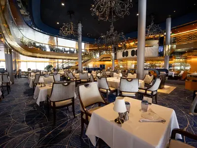 Elegant gedeckte Tische im großzügigen, mehrstöckigen Hauptrestaurant an Bord der Volendam mit klassischen Kronleuchtern.