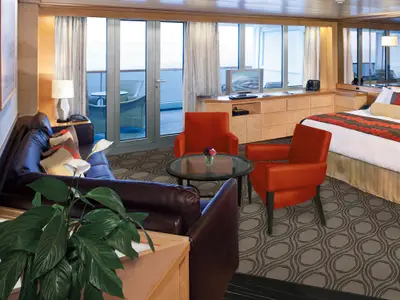 Elegante und gemütliche Suite an Bord der Volendam mit dunklem Ledersofa, zwei roten Sesseln, Balkon und Bett.