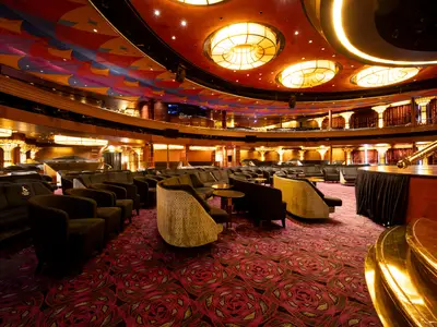 Blick in das World Stage Theater an Bord der Volendam mit stilvollen Sesseln, gemustertem Teppich und warmer Deckenbeleuchtung.