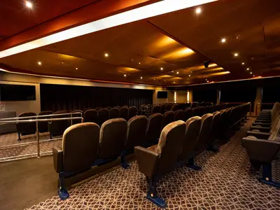 Innenansicht des gemütlichen Wajang Theaters an Bord der Volendam mit Reihen von dunklen Kinosesseln unter warmer Beleuchtung.