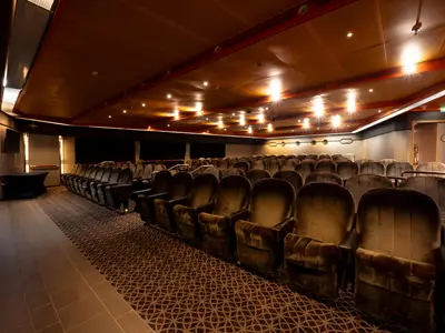 Blick in das Wajang-Theater an Bord der Volendam mit Reihen von gepolsterten Kinosesseln, gemustertem Teppich und warmer Deckenbeleuchtung.