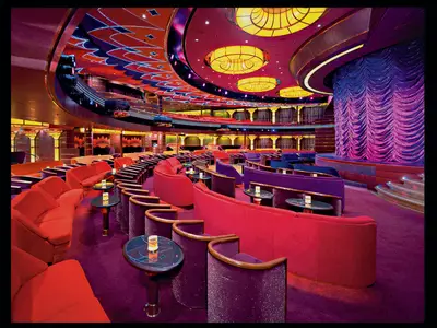 Blick in das Show-Theater an Bord der Volendam mit lila und roten Sesseln, kleinen Tischen und einer Bühne mit violettem Vorhang.