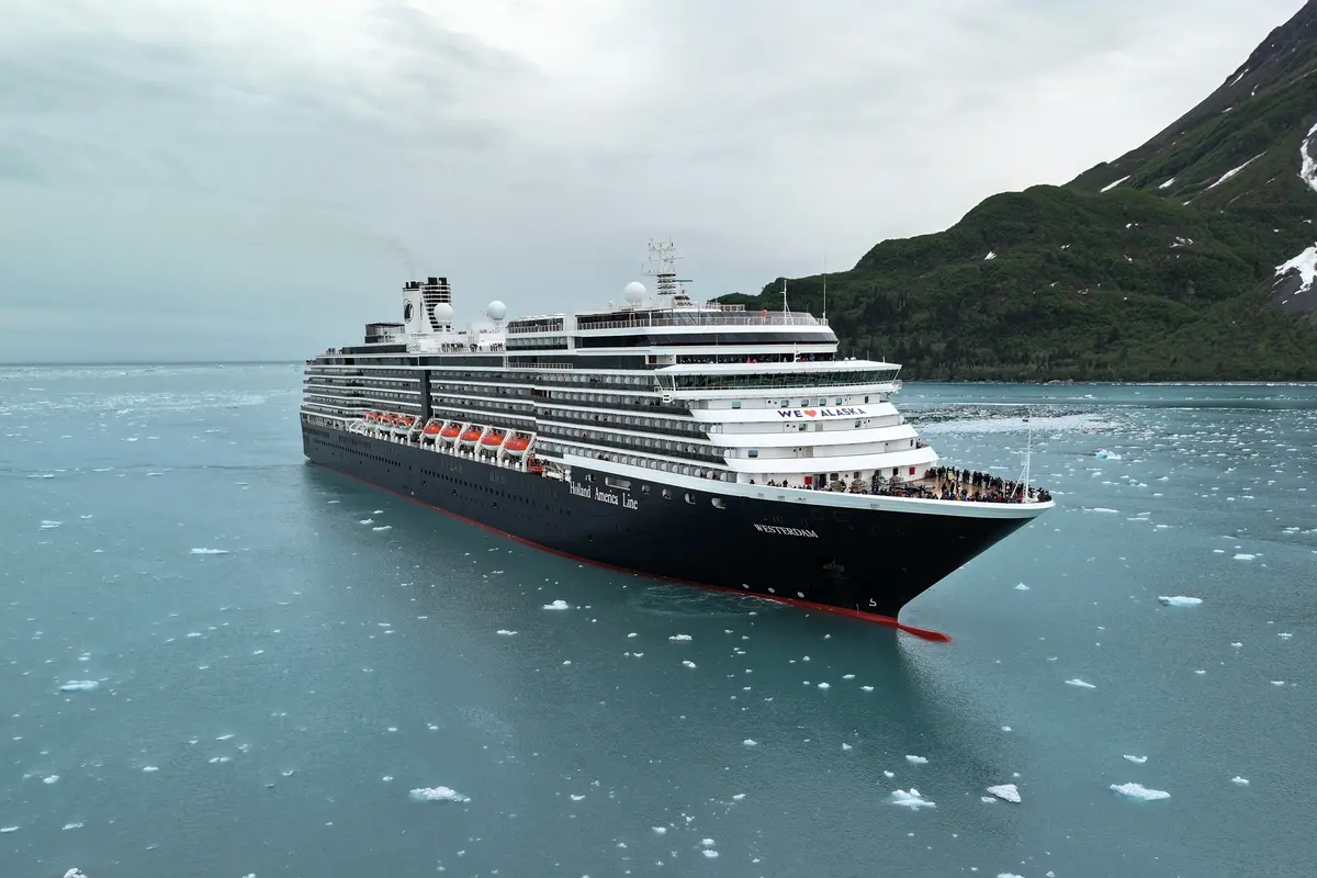 Drohnenaufnahme der Westerdam, die durch eisiges Wasser vorbei an bewaldeten Bergen in Alaska fährt.