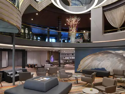 Blick in das moderne, elegant gestaltete Atrium an Bord der Westerdam mit gemütlichen Sitzgruppen, Kunstwerken und einer Treppengalerie.