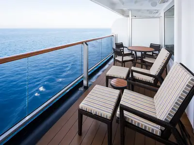 Ein geräumiger Balkon an Bord der Westerdam mit bequemen Sesseln, Fußhockern und Holztischen vor dem tiefblauen Meer.