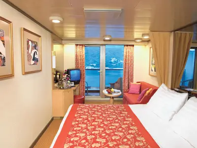 Eine hell eingerichtete Balkonkabine an Bord der Westerdam mit einem Doppelbett im Vordergrund, einem roten Sofa und Blick auf das Meer.