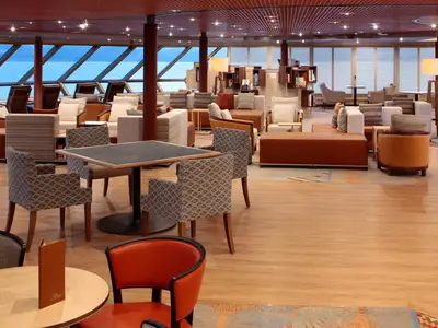 Der stilvolle Loungebereich Explorations Cafe an Bord der Westerdam bietet gemütliche Sessel, Holzboden und große Panoramafenster mit Blick aufs Meer.