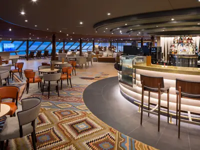 Blick in das moderne Explorations Café an Bord der Westerdam mit Bar, Barhockern, Sesseln und Meerblick durch die Fensterfront.