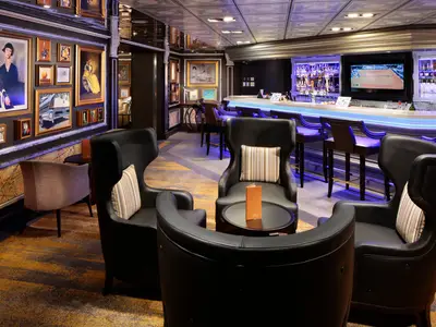 Die Gallery Bar an Bord der Westerdam mit bequemen Sesseln, einer beleuchteten Bar im Hintergrund und zahlreichen Gemälden an der Wand.
