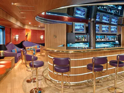 Blick auf die Sports Bar an Bord der Westerdam mit einer geschwungenen Holztheke, lila Barhockern und mehreren Fernsehbildschirmen.