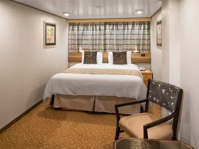 Einblick in eine komfortable Innenkabine an Bord der Westerdam mit Doppelbett, gemustertem Sessel und gestreiftem Vorhang im Hintergrund.