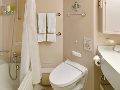Ein helles, sauberes Badezimmer an Bord der Westerdam mit Toilette, Waschbecken, Dusche und weißen Handtüchern.