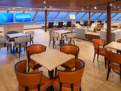 Stilvoll eingerichtete Lounge an Bord der Westerdam mit gemütlichen Sitzgruppen, Holzfußboden und großen Panoramafenstern mit Blick aufs Meer.