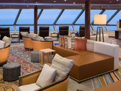 Einladender Aufenthaltsbereich an Bord der Westerdam mit bequemen Polstermöbeln und freier Sicht auf das Meer durch schräge Fensterfronten.