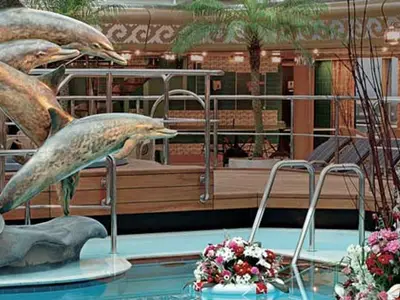 Der Lido-Pool an Bord der Westerdam zeigt bronzene Delfinskulpturen und bunte Blumengestecke am Beckenrand.