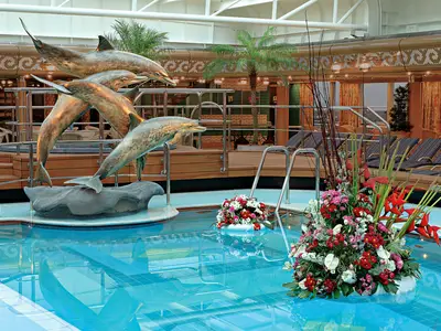 Poolbereich an Bord der Westerdam mit einer großen bronzenen Delfinskulptur und schwimmenden Blumengestecken im blauen Wasser.
